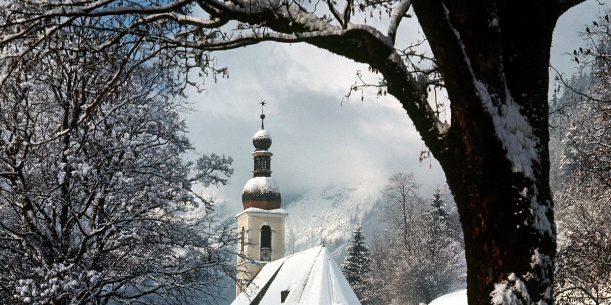 Die Kirche von Ramsau bei Berchtesgaden inmitten einer romatisch verschneiten Landschaft.