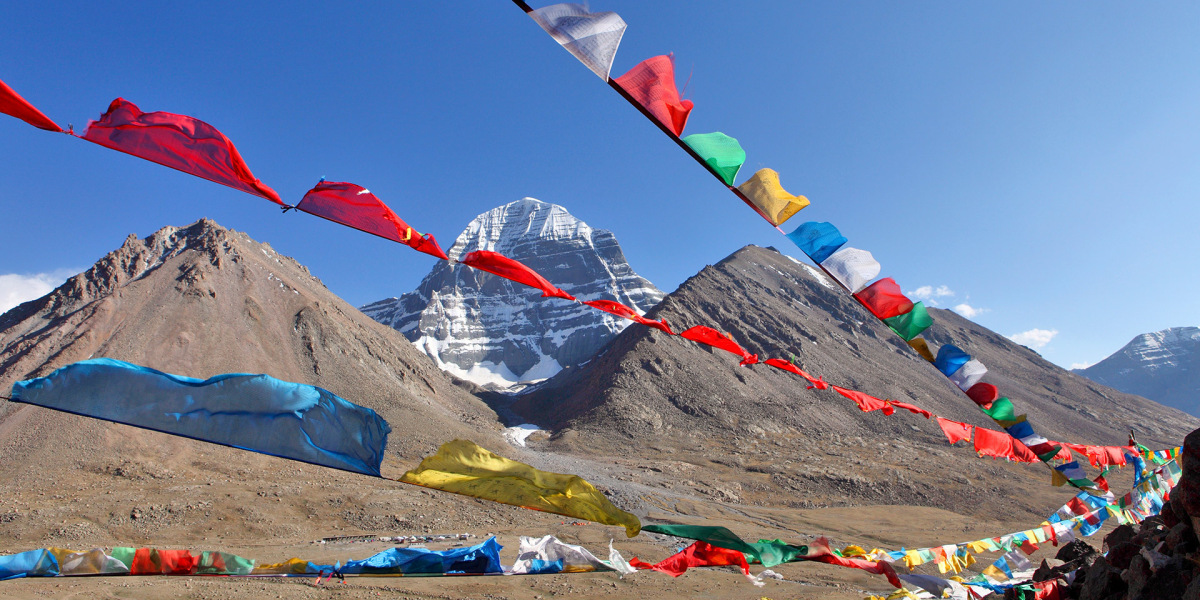 Typisch Tibet: Gebetsfahnen flattern im Wind. Im Hintergrund leuchtet die horizontal geschichtete Stein-Pyramide des Kailash (6638 m) mit ihrer Schneekuppe. 