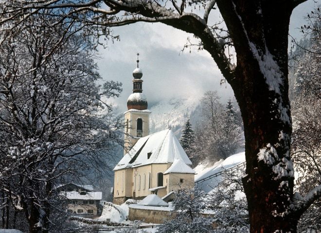 Die Kirche von Ramsau bei Berchtesgaden inmitten einer romatisch verschneiten Landschaft.